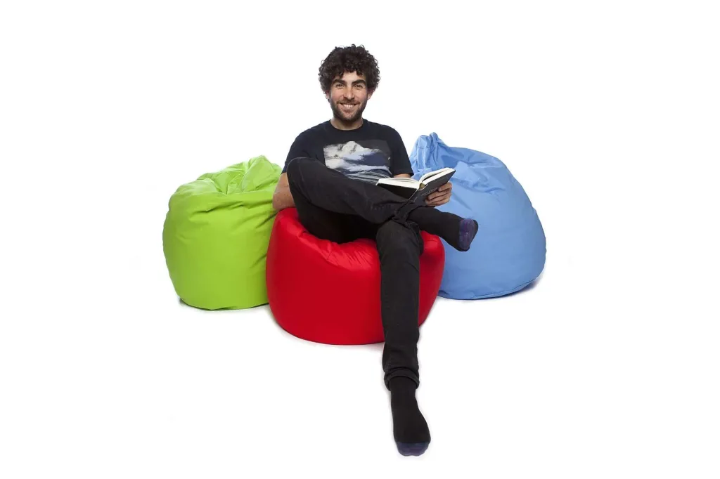 Man sitting cross-legged on a red cotton bean bag reading a book, flanked by lime and royal blue cotton bean bags.