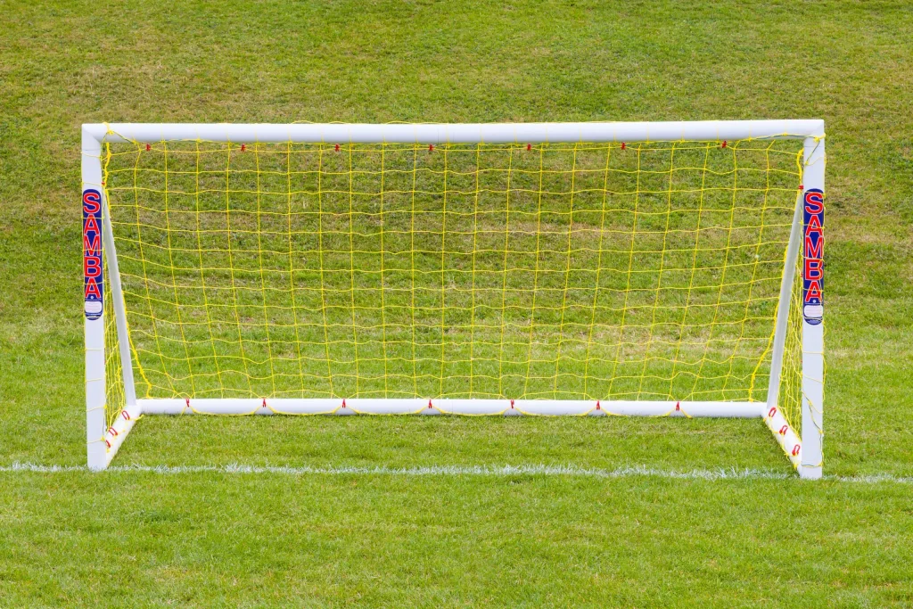 White uPVC freestanding goal with yellow netting and SAMBA labels, standing on green grass.