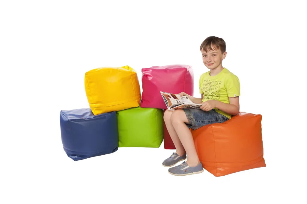 Child seated on an orange faux leather square bean pod reading a magazine beside four stacked faux leather pods in yellow, pink, green and blue.