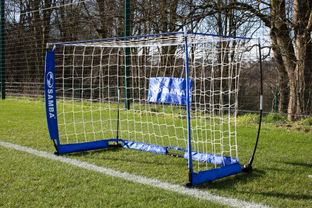 Blue Samba speed goal with white net, taped crossbar and rubber feet standing on grass.