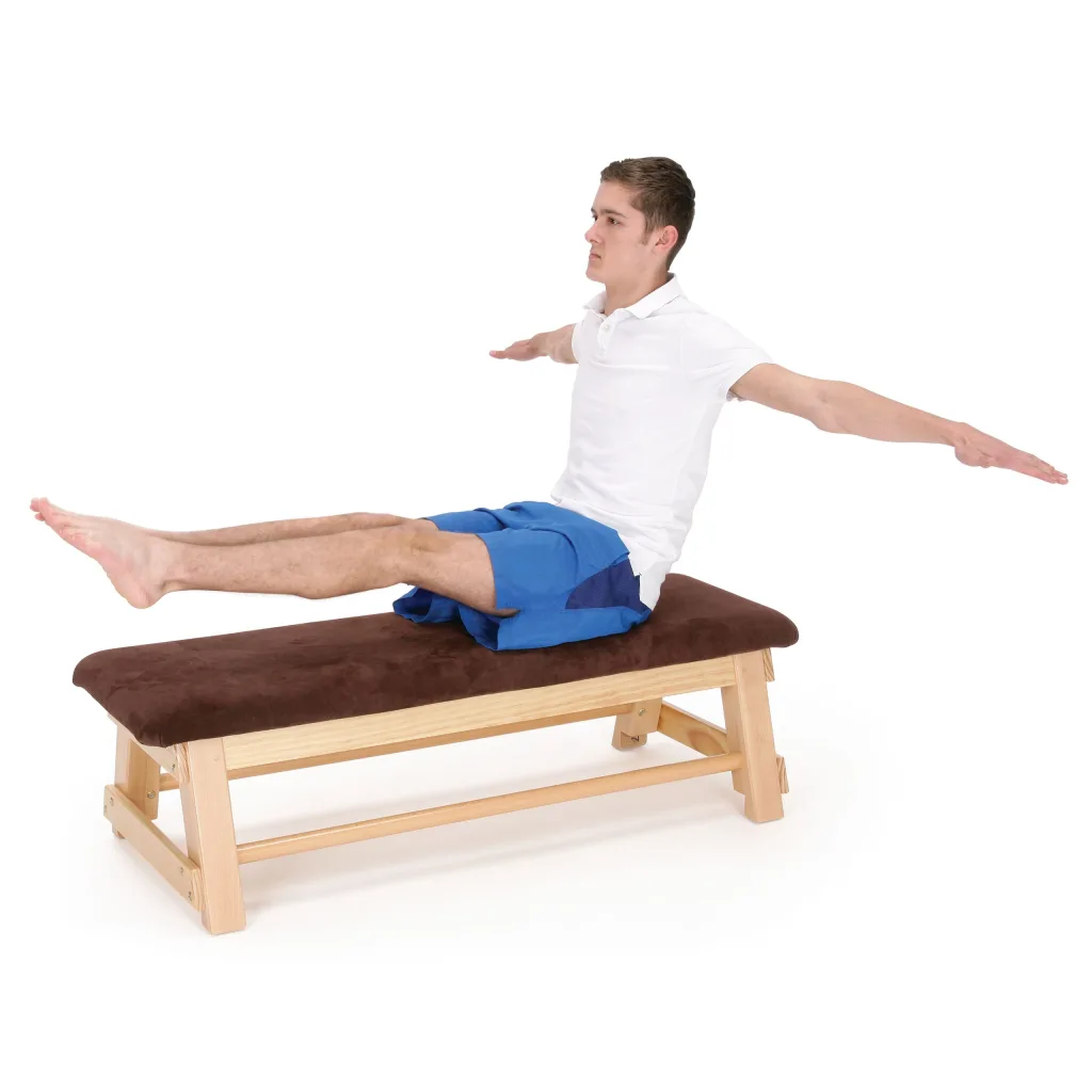 A man in a white polo and blue shorts sits on a wooden bar box with a brown hide top, legs extended and arms outstretched.