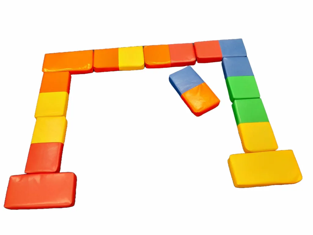 High-density foam dominoes with wipe-clean covers in a mixture of 4 random colours arranged in an open arch, one tile tilted inside.