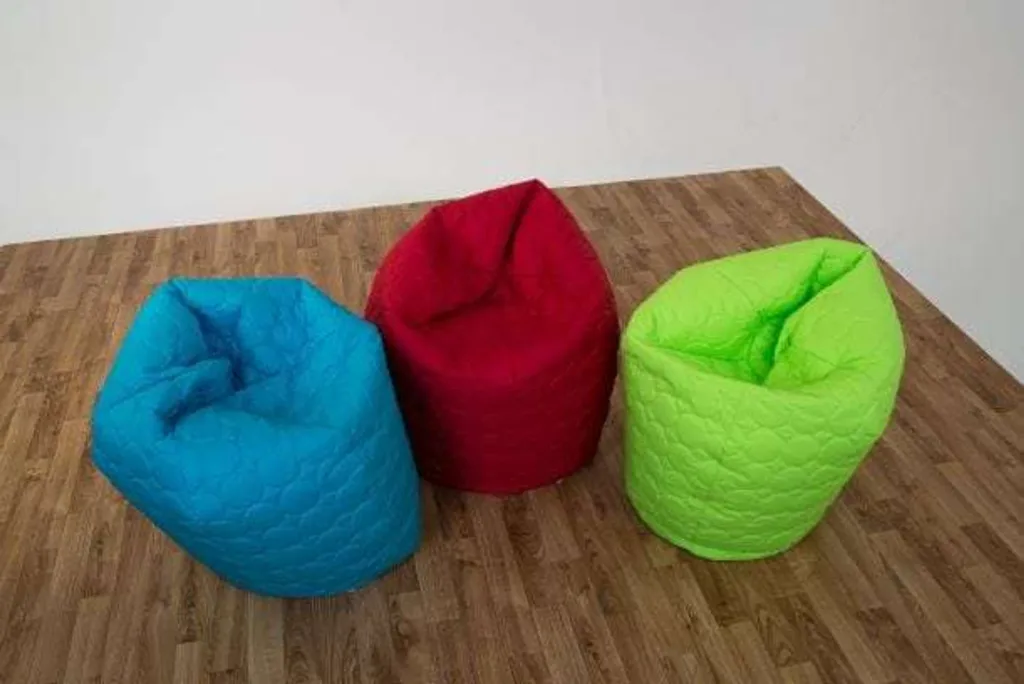 Three padded child bean bags in aqua, red and lime arranged on a wood-look floor.