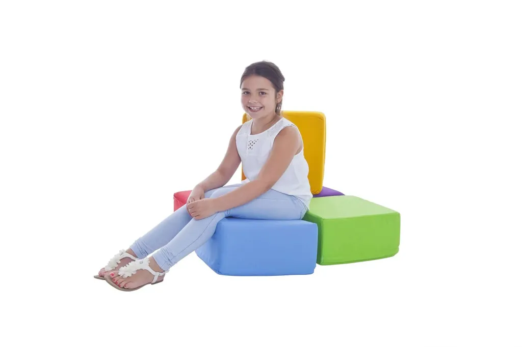 Young girl smiling while seated on a set of five cotton square foam seating pods in bright colors, with one used as a yellow backrest.