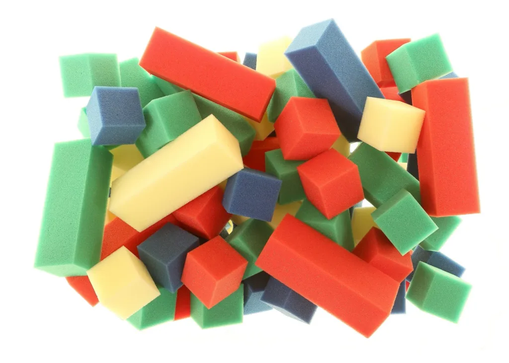 Pile of multicolored foam rectangular and cube blocks in red, green, blue, and yellow on a white background.