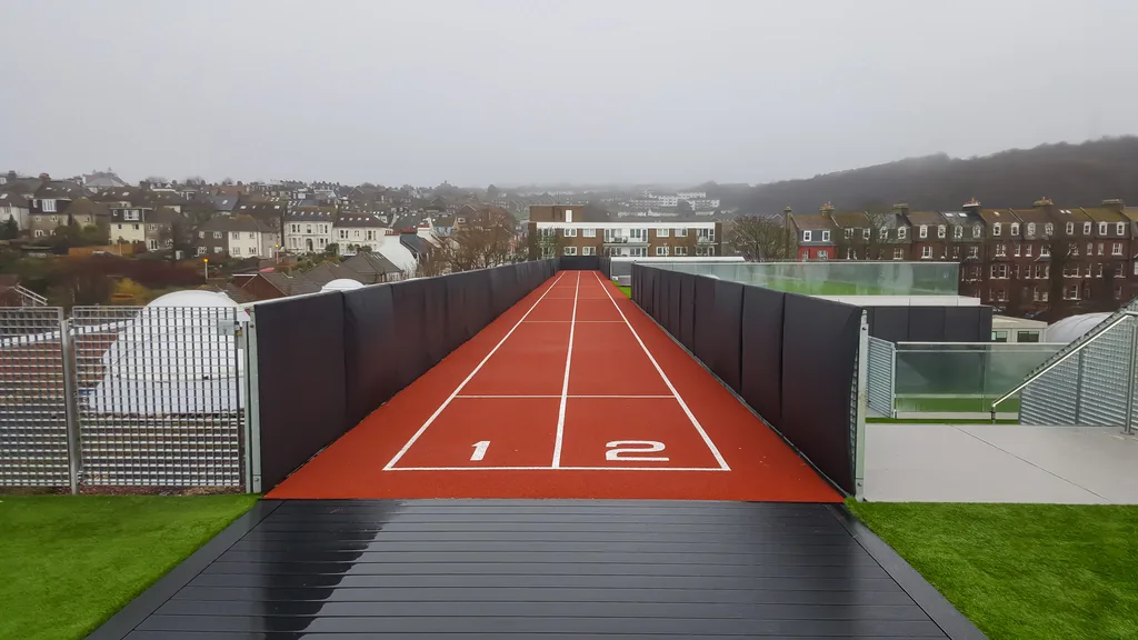 Rooftop red two-lane running track marked 1 2 at the start with black safety padding along both sides and city buildings beyond.