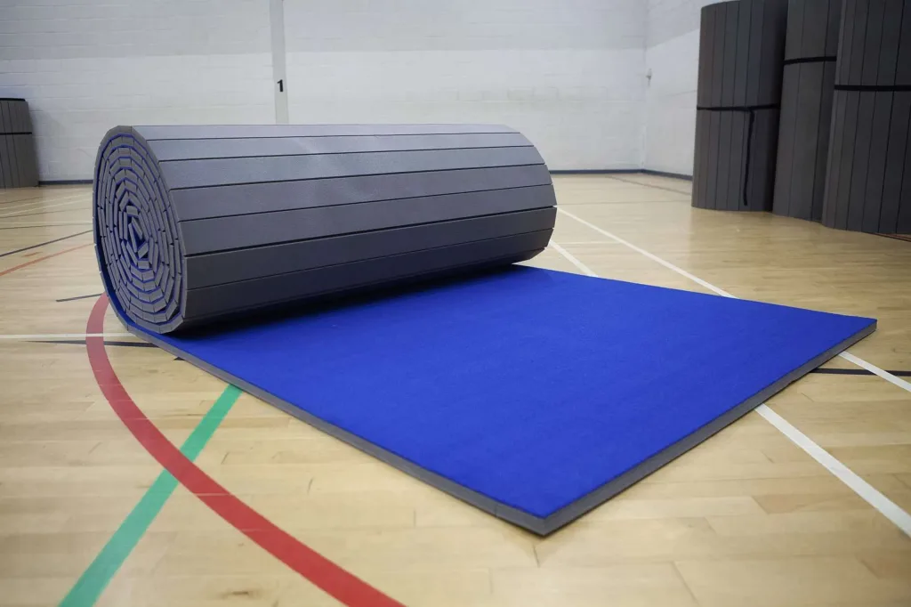 Blue carpet roll-out mat with a light grey XPE foam core partially unrolled on a wooden gym floor.