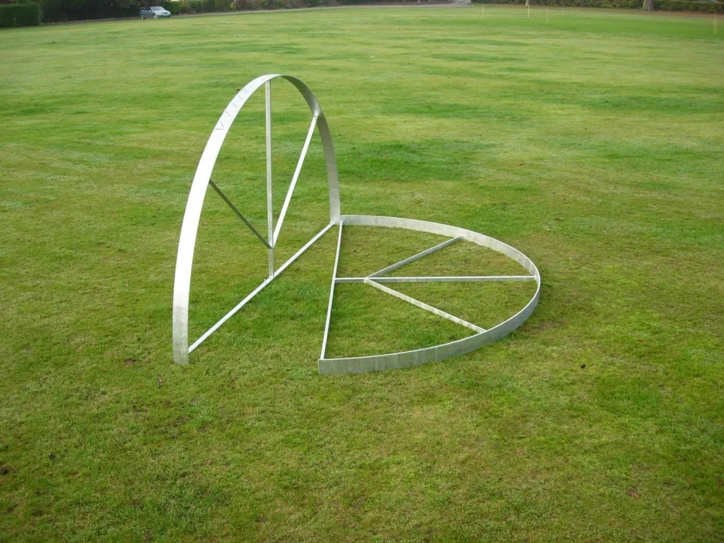 Steel throwing circle on mowed grass, one semicircular rim standing upright with radial supports and the other half laid flat.