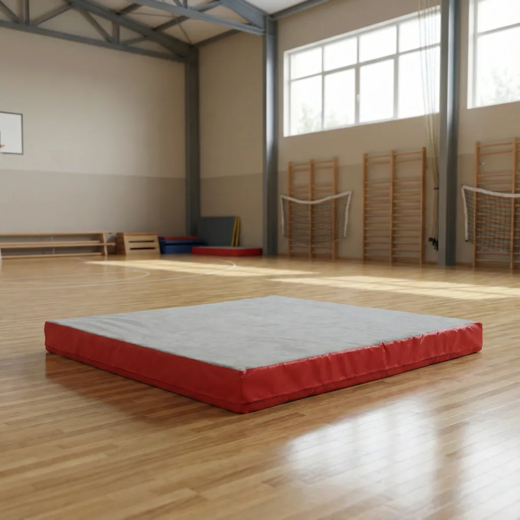 Rectangular crash mat with a light gray jersey fabric top and red PVC sides resting on a wooden gym floor.