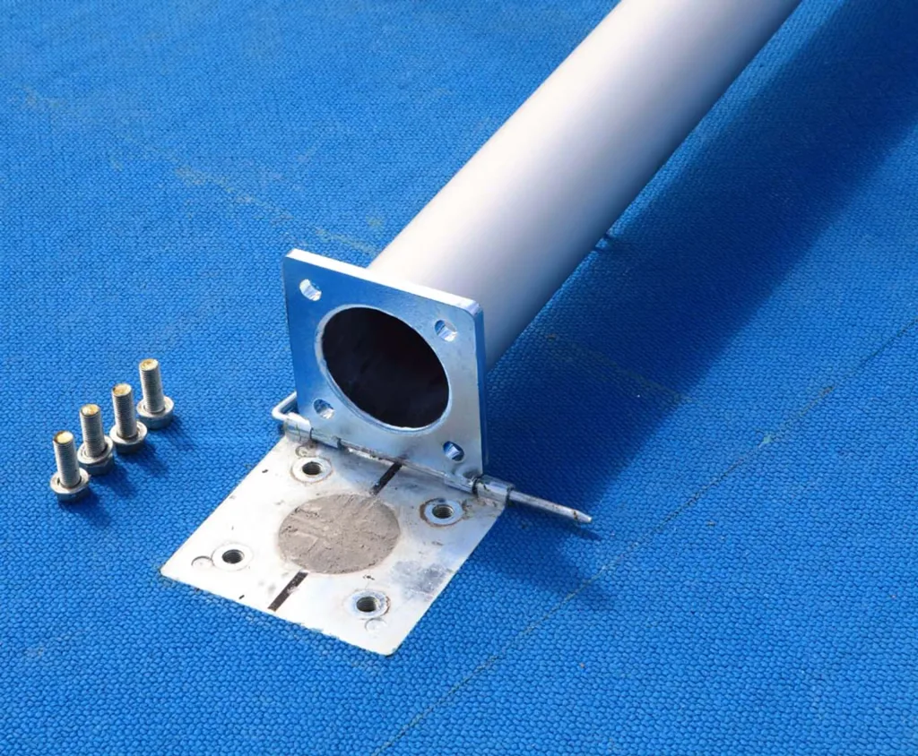 Aluminium round post with square flange and hinge-mounted base plate, four bolts beside it, resting on a blue textured surface.