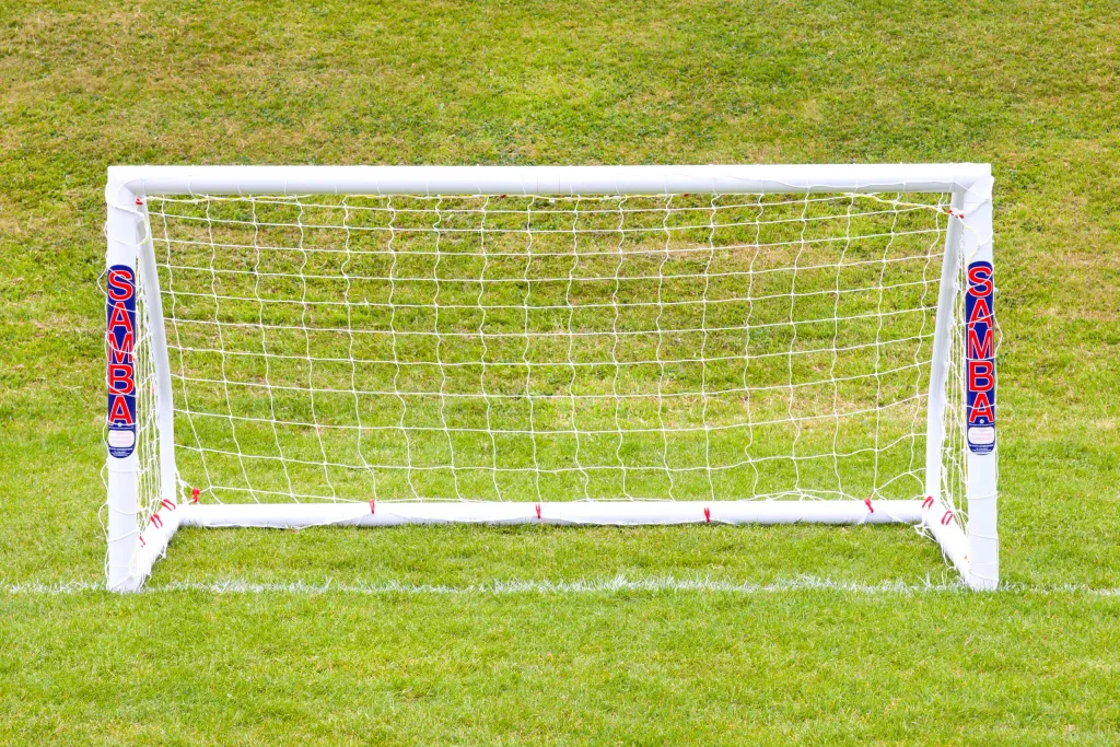 White freestanding uPVC soccer goal with knotted net on grass and vertical red-and-blue labels reading SAMBA on each post.