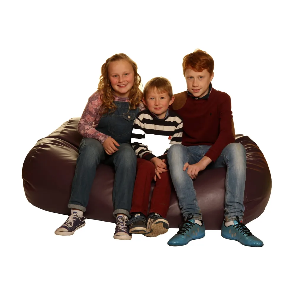 Three children sitting together on a faux leather child bean settee.