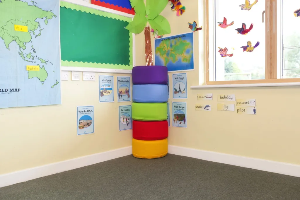 Stacked set of five cotton foam seating pods in purple, light blue, green, red and yellow in a classroom corner with posters reading "Visit Spain" and "Visit Australia".