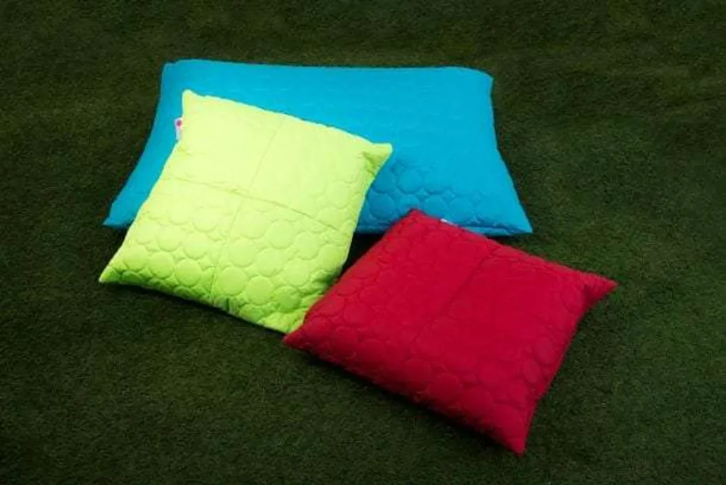 Three padded floor cushions in aqua, lime and red with a circular quilted pattern on a dark green carpet.