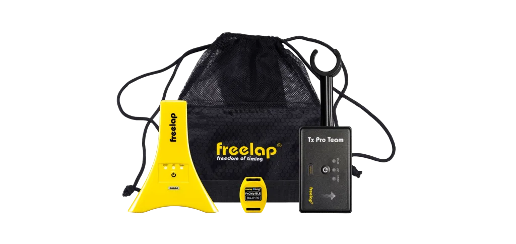 Yellow triangular timing unit, small yellow chip labeled FxChip BLE BA-0139, black Tx Pro Team box, and black mesh drawstring bag reading freelap freedom of timing.