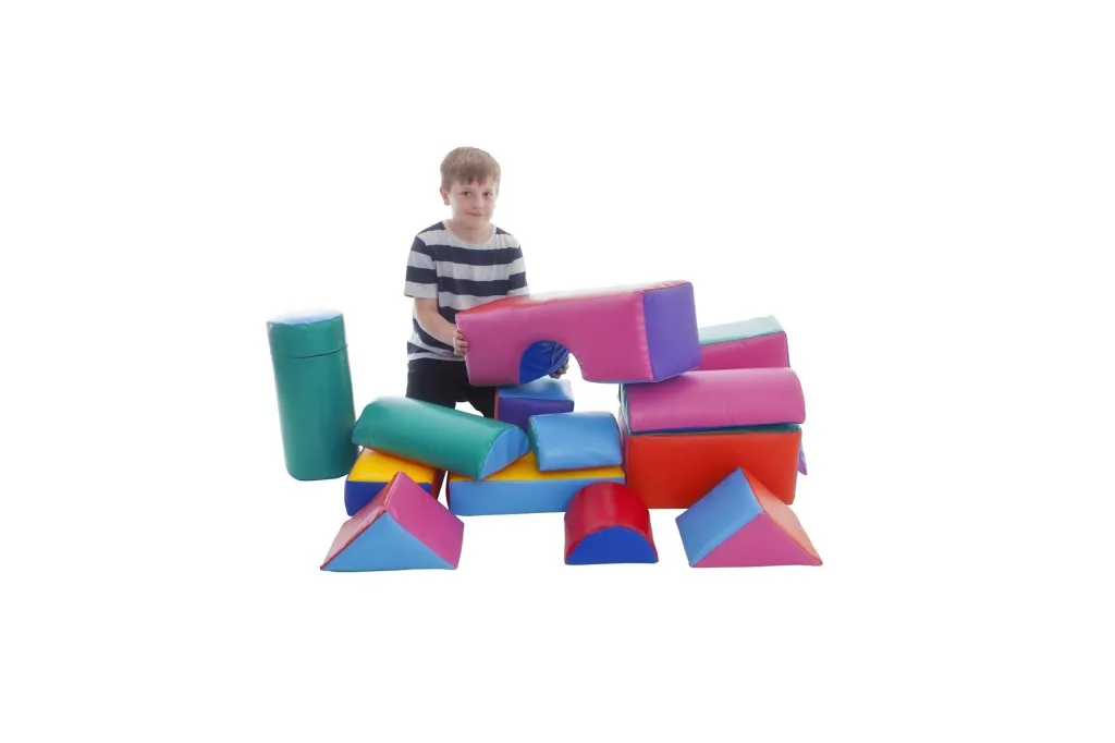Child standing behind 14 assorted building shapes in random colours, including blocks, wedges, cylinders and semicircles.