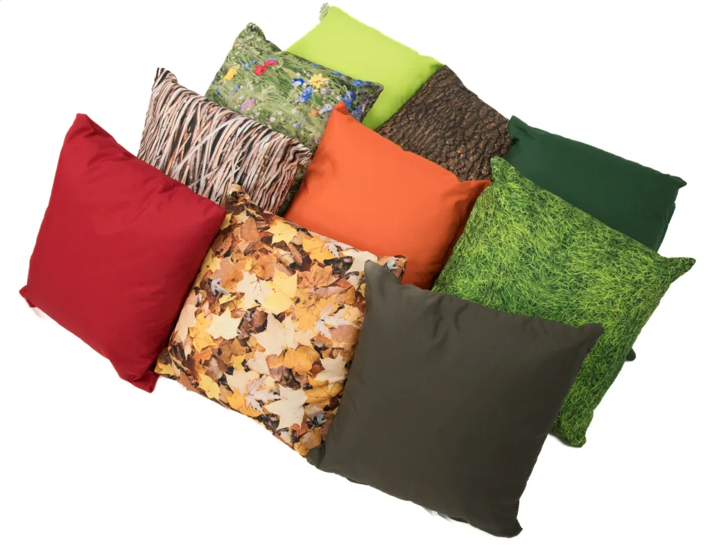 Ten coordinating scatter cushions with seasonal nature-print patterns and solid colours, arranged overlapping in a casual pile.