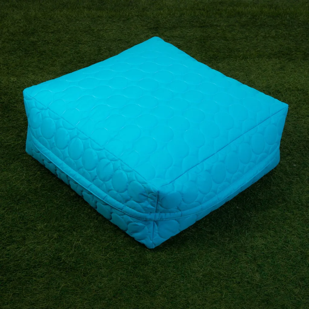 Padded child square bean bag with circular quilted stitching resting on grass.