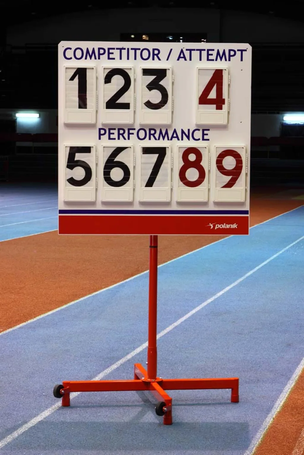 White freestanding scoreboard on a red wheeled stand at an indoor track, headings COMPETITOR / ATTEMPT and PERFORMANCE with flip numbers 1 2 3 4 5 6 7 8 9.
