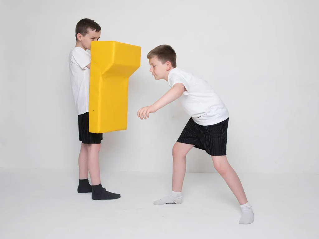 Two boys practice tackling with a yellow rucking shield with a sewn heavy duty 610gsm PVC cover and shock-absorbing foam core.