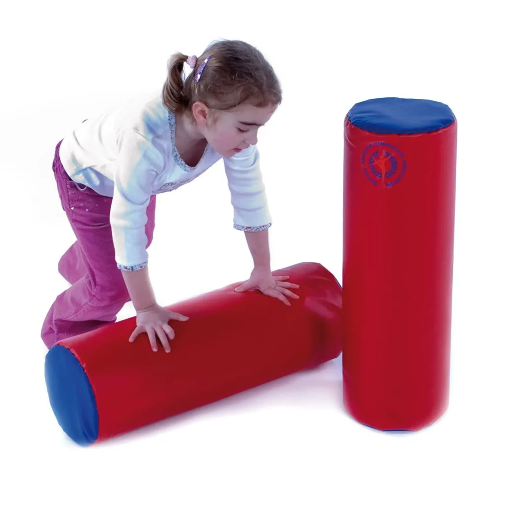 A young girl kneeling and leaning on two red soft-play foam cylinders with blue ends against a white background.