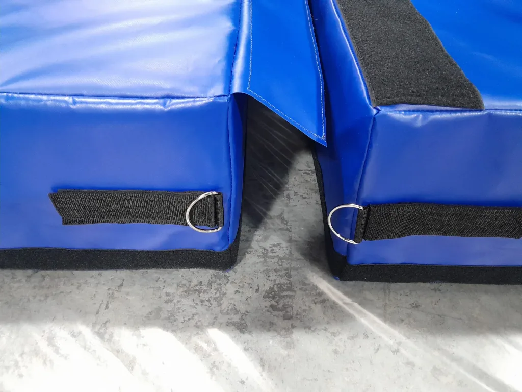 Two blue landing mat modules with black hook-and-loop strips and silver D-rings, their covers parted to show a narrow gap to the floor.