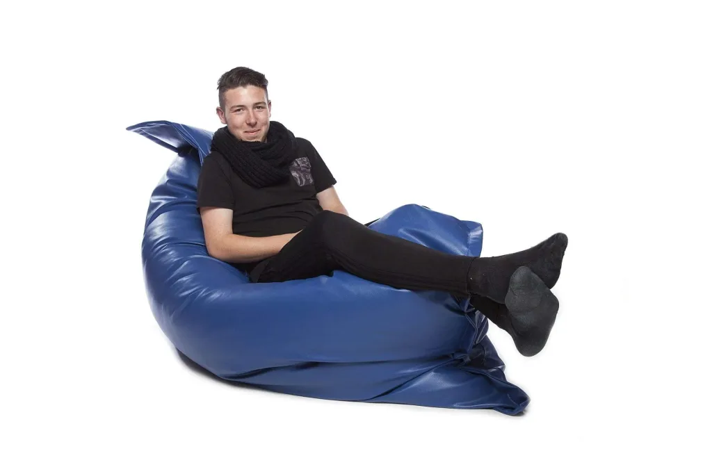 Young adult reclining with legs extended on a royal blue faux leather floor cushion against a white background.