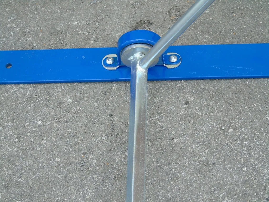 Steel hurdle base with blue padded top board, angled steel support leg and wheel assembly resting on rough asphalt.