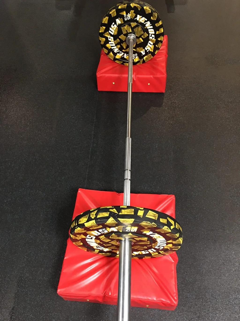 Red fire-retardant PVC weightlifting drop pads supporting a barbell with black-and-yellow weight plates.