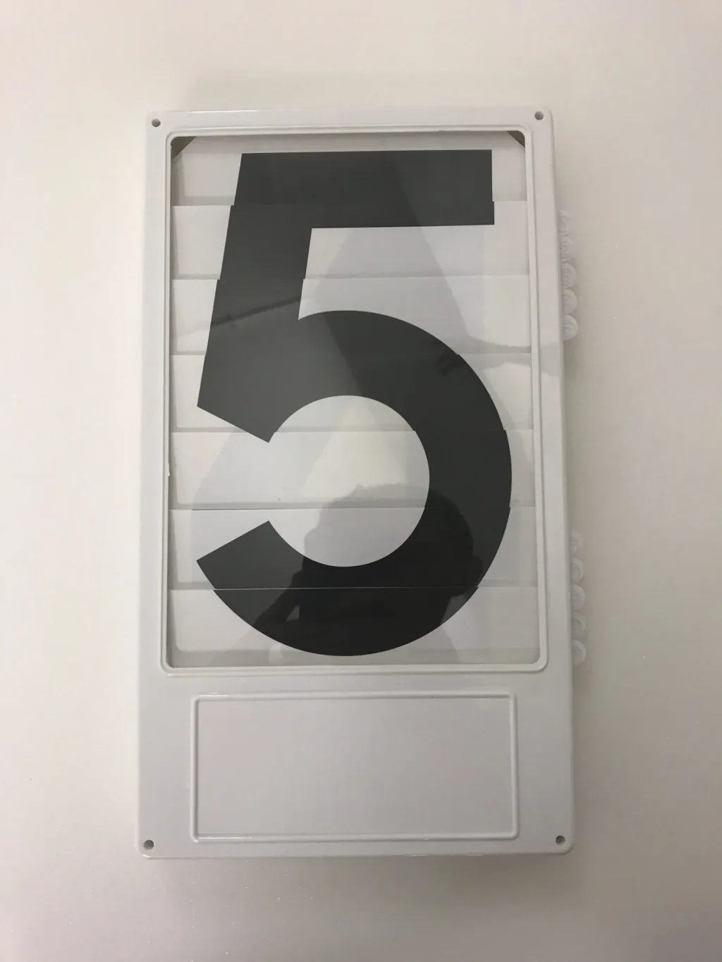 Plastic number board with slatted panels and side levers displaying the number 5.