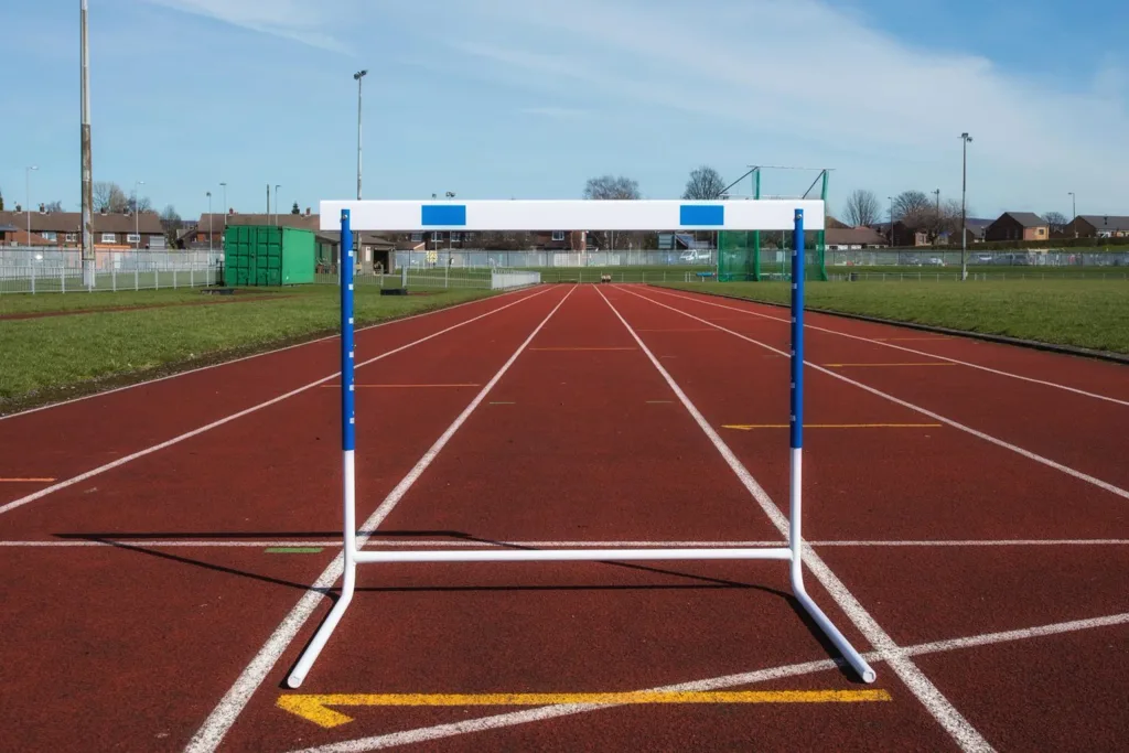 White and blue training hurdle with UPVC top board positioned on a red outdoor running track.