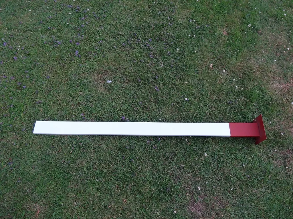 Cantabrian finishing post with a white powder-coated steel bar and red base plate lying on grass, FINISH printed on the post.