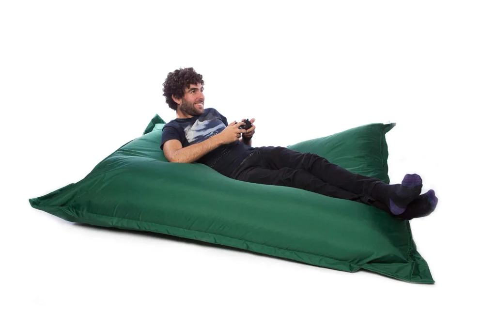 Man reclining on a large green polyester floor cushion, holding a video game controller.