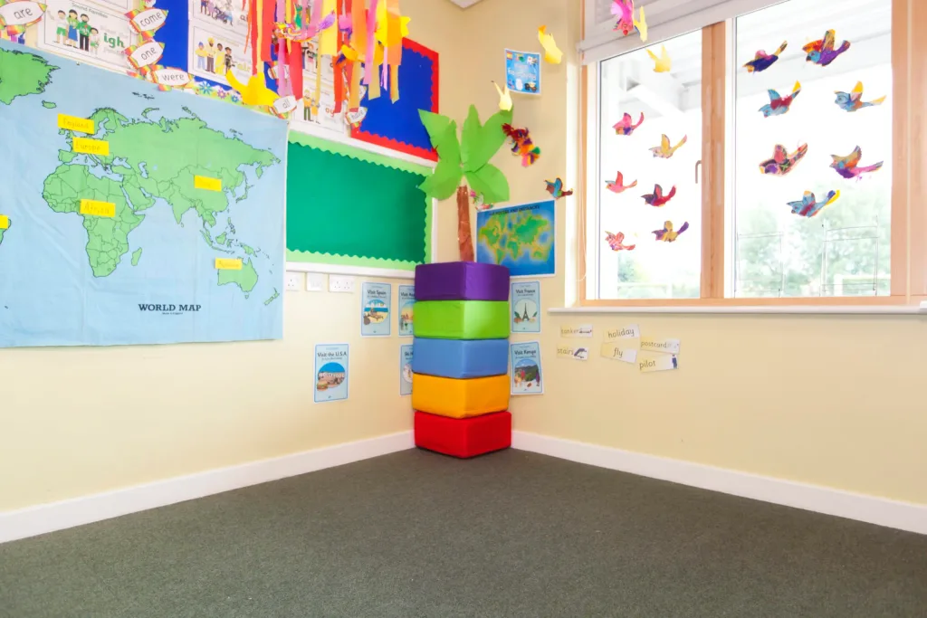 Stack of five cotton square foam seating pods (red, orange, blue, green, purple) in a classroom corner beneath a map labeled WORLD MAP.