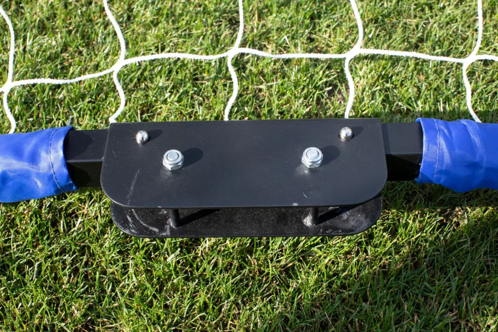 Black metal base plate with two bolts and blue padded sleeves securing a taped crossbar to a white goal net on grass.