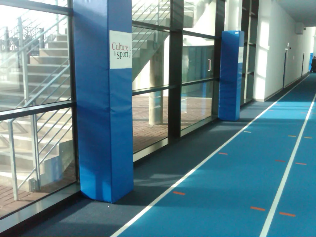Royal blue square post pads of polyurethane foam with heavy duty PVC cover along an indoor running track; sign reads Culture : sport.