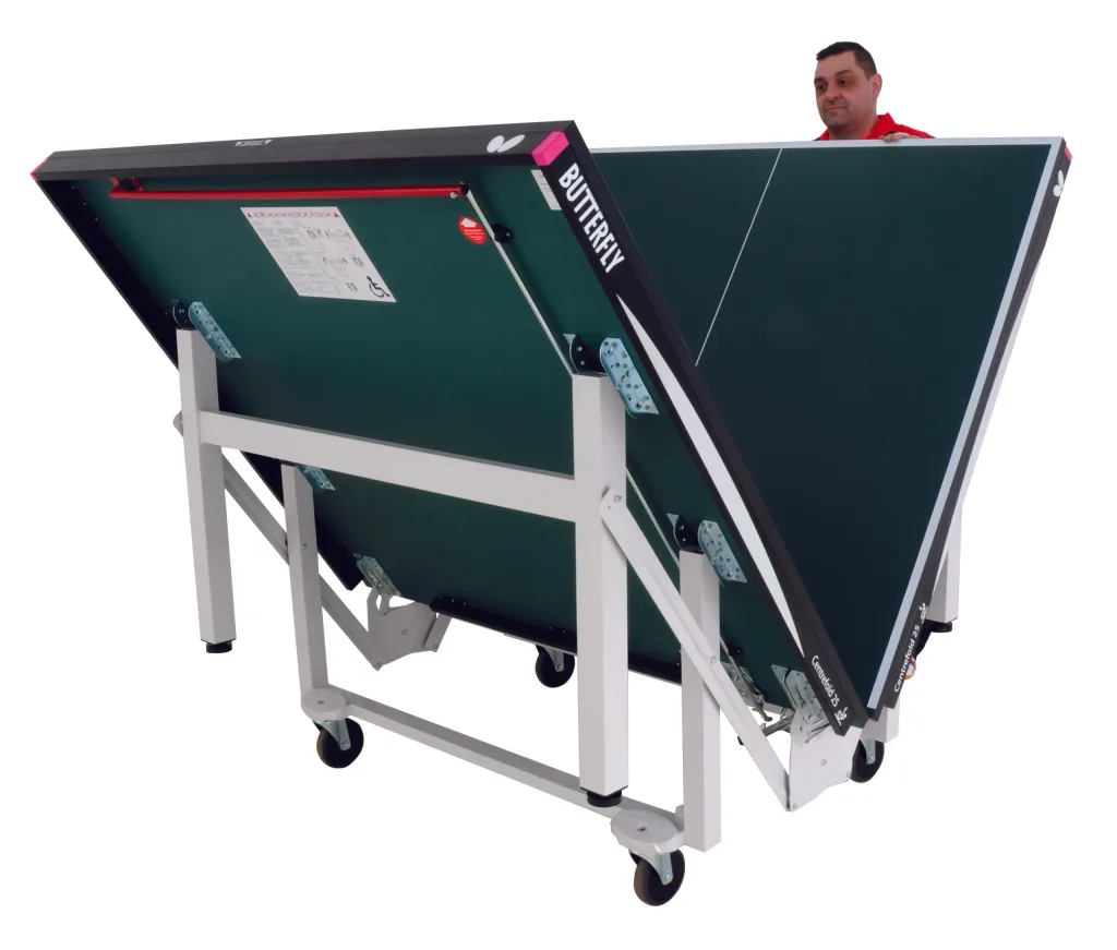 Folded Centrefold 25 table tennis table with green top, light silver legs, magenta corner pieces, wheels and a man peeking over an end.