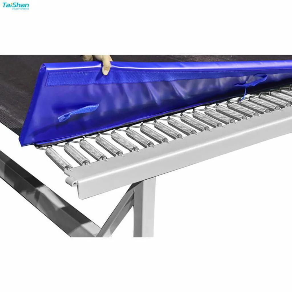 Training fast track trampoline section with frame protection padding lifted to show PVC-coated nylon mesh, steel springs, and welded carbon steel frame.