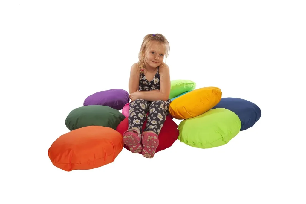 Young girl sitting on a pile of ten round polyester fibre-filled scatter cushions in assorted bright colours against a white background.