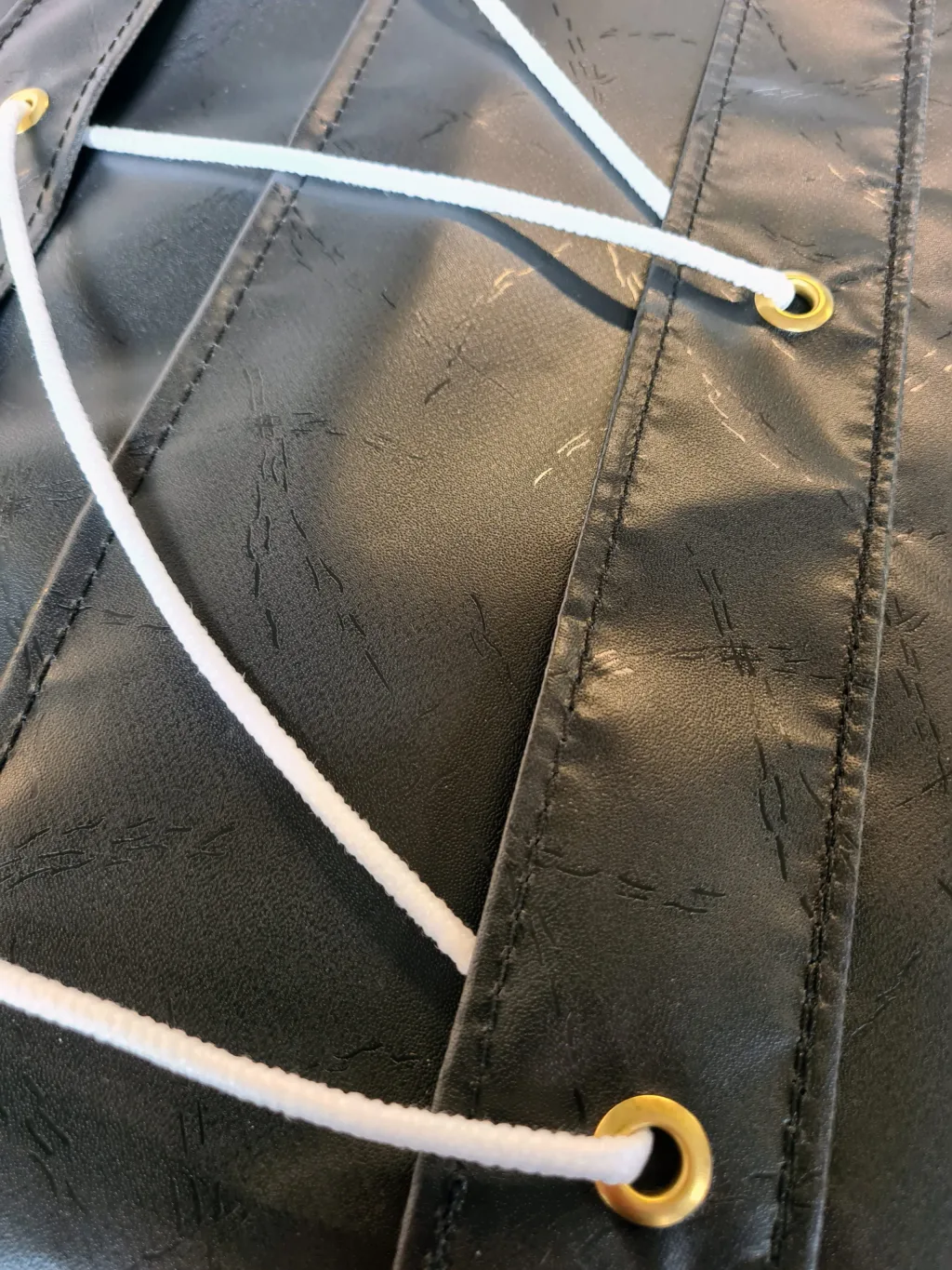 Black fire-retardant PVC keg mat with stitched panels, brass eyelets, and a white cord threaded through them.