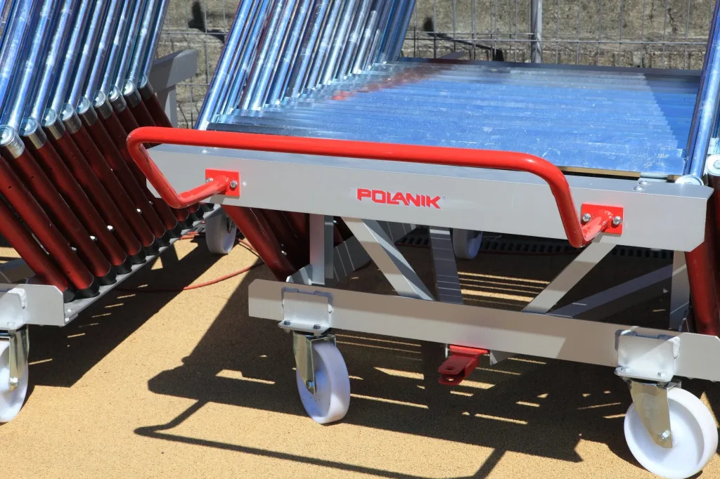 Silver anodised aluminum hurdle cart with a red ergonomic handle and white caster wheels holding stacked metal hurdles.