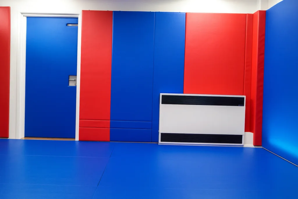 Room with blue padded floor and alternating red and blue wall pads, a blue padded door, and a white wall-mounted heater.