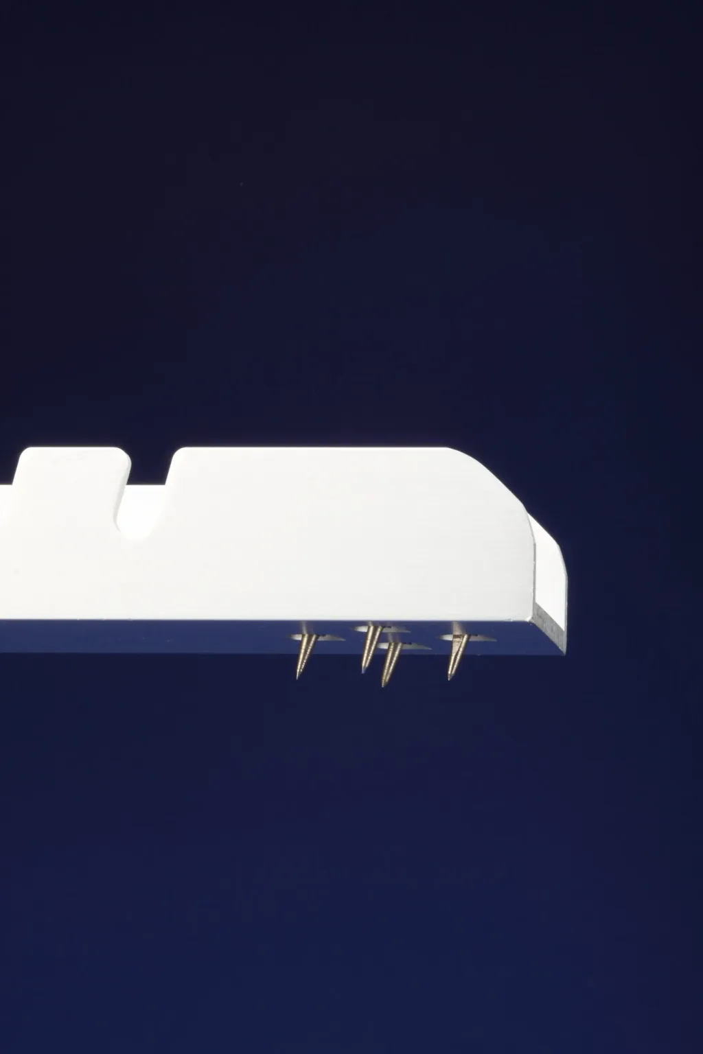 Galvanised steel competition starting block footplate with four metal spikes visible beneath against a dark blue background.