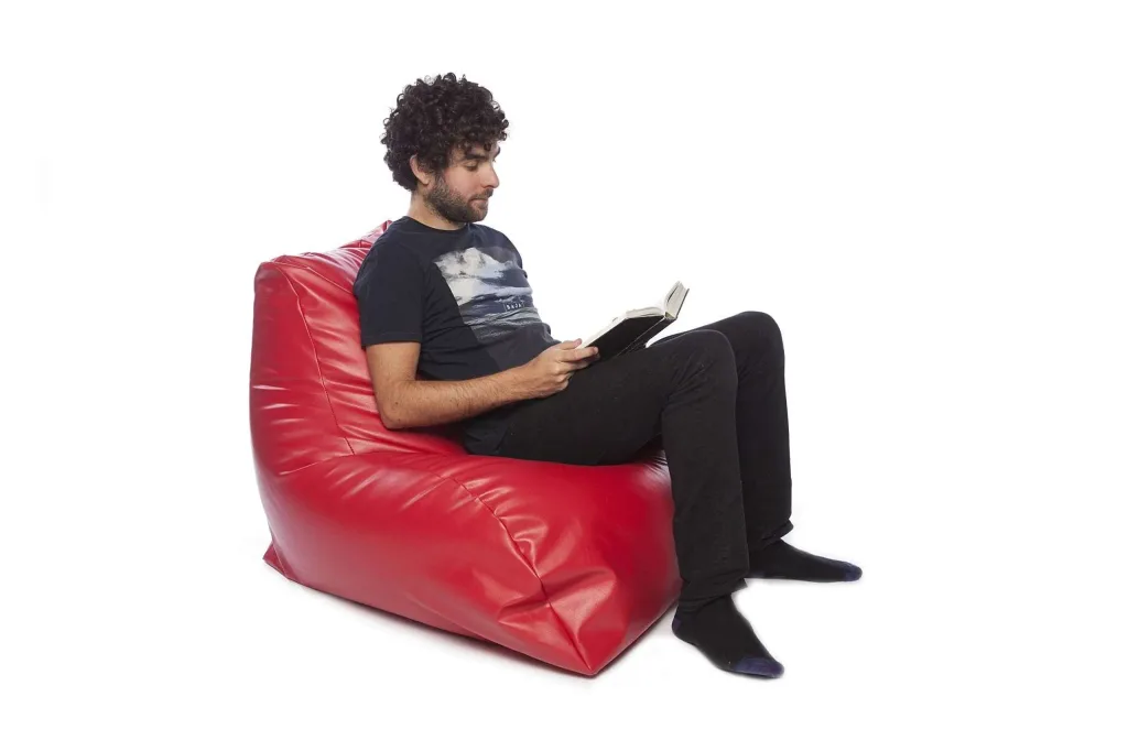 Man with curly hair sitting and reading on a red faux leather PVC bean chair with an extended back.