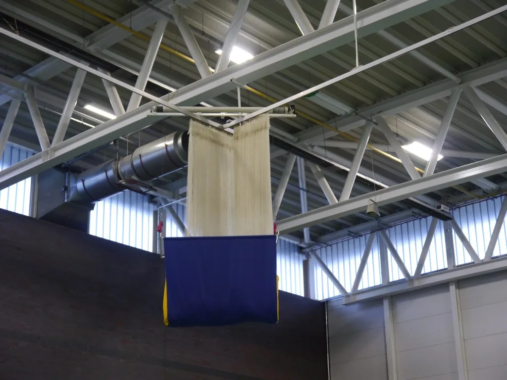 Green dividing curtain with a high green sight screen sewn to its base suspended from a ceiling track in an indoor sports hall.