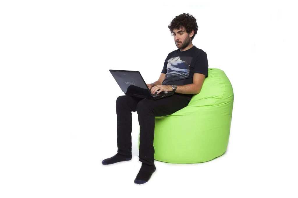 Adult man sitting on a lime cotton bean chair using a laptop against a white background.