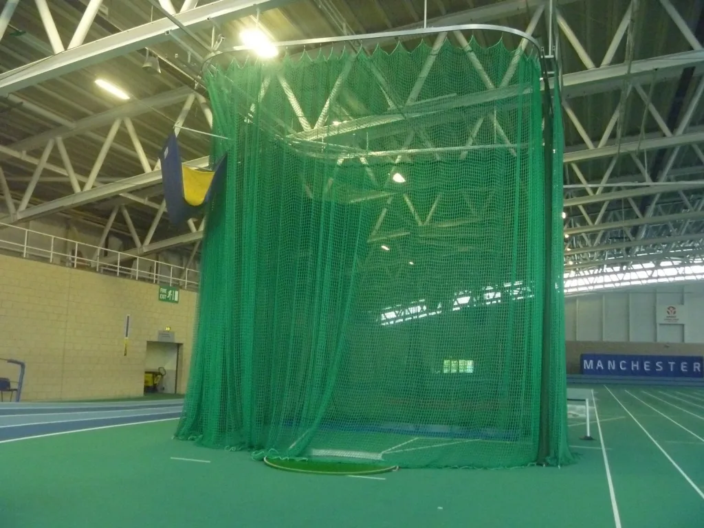 Green netted indoor throws cage with the word MANCHESTER on a distant wall.