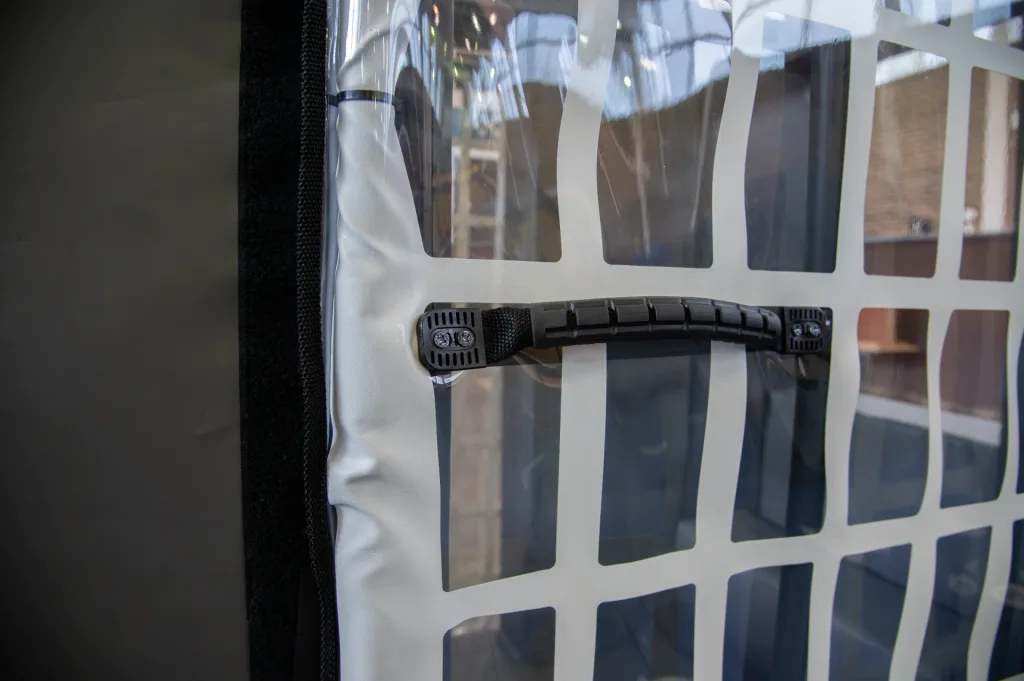White PVC-covered training cage panel with reinforced foam core, clear square windows, black plastic handle and black Velcro edge.