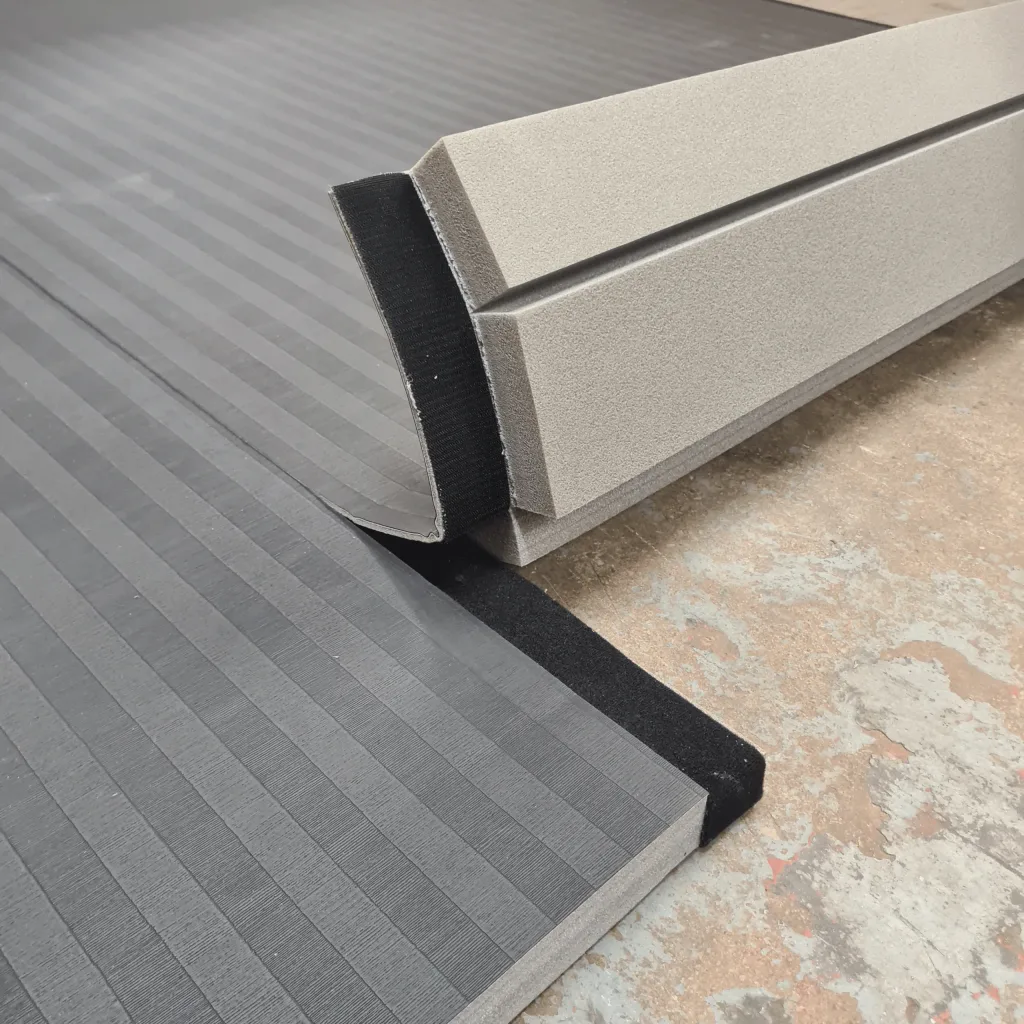 Grey PVC roll-out mats with low-profile tatami emboss and a black hook-and-loop connecting edge on foam backing, partially unrolled on a concrete floor.