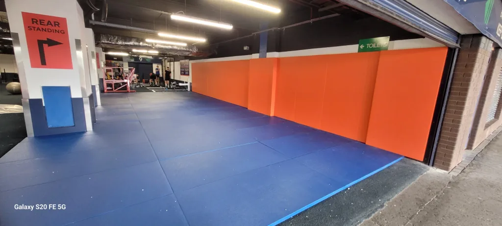 Blue mats cover the floor beside orange wall pads in a gym, with a red sign reading REAR STANDING and watermark Galaxy S20 FE 5G.
